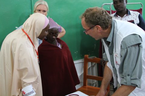 En manlig läkare konverserar med ett barn, ärrat av noma.