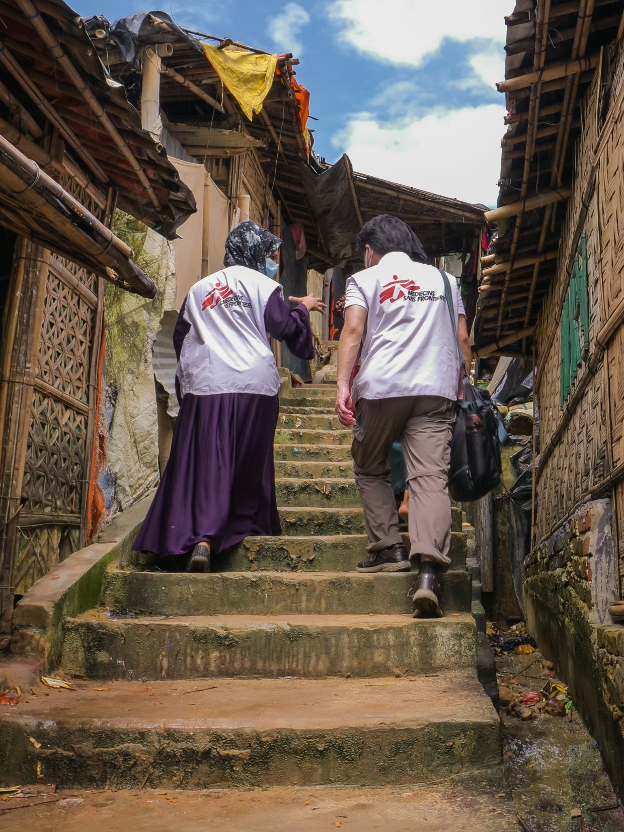 Två medarbetare med Läkare Utan Gränsers logga på ryggarna går upp för en trappa i Cox's Bazar.