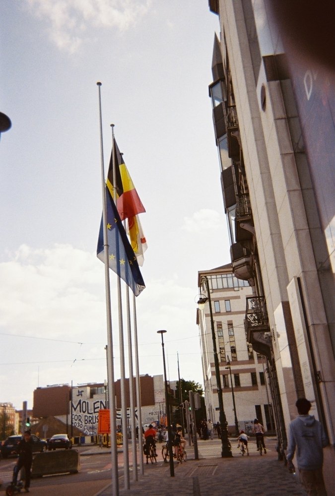 Flaggstänger med flaggor framför byggnader och gata.