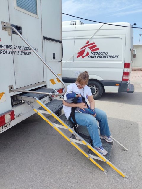 Mia sitter med en bebis i famnen utanför vår mobila klinik