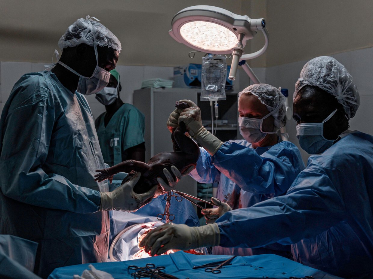 förlossning med kejsarsnitt, en kirurg håller upp det nyfödda barnet under en operationslampa