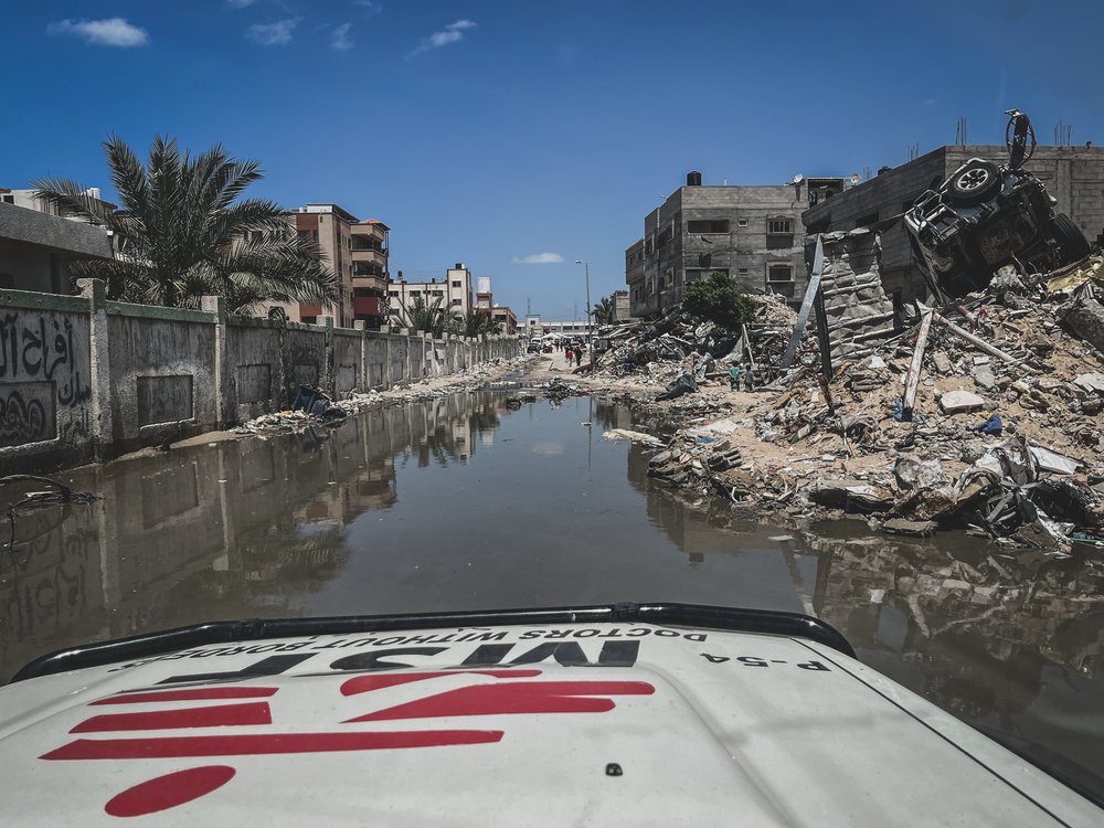 En av Läkare Utan Gränsers bilar kör på en väg fylld av vatten och runt om syns massa förstörda hus.