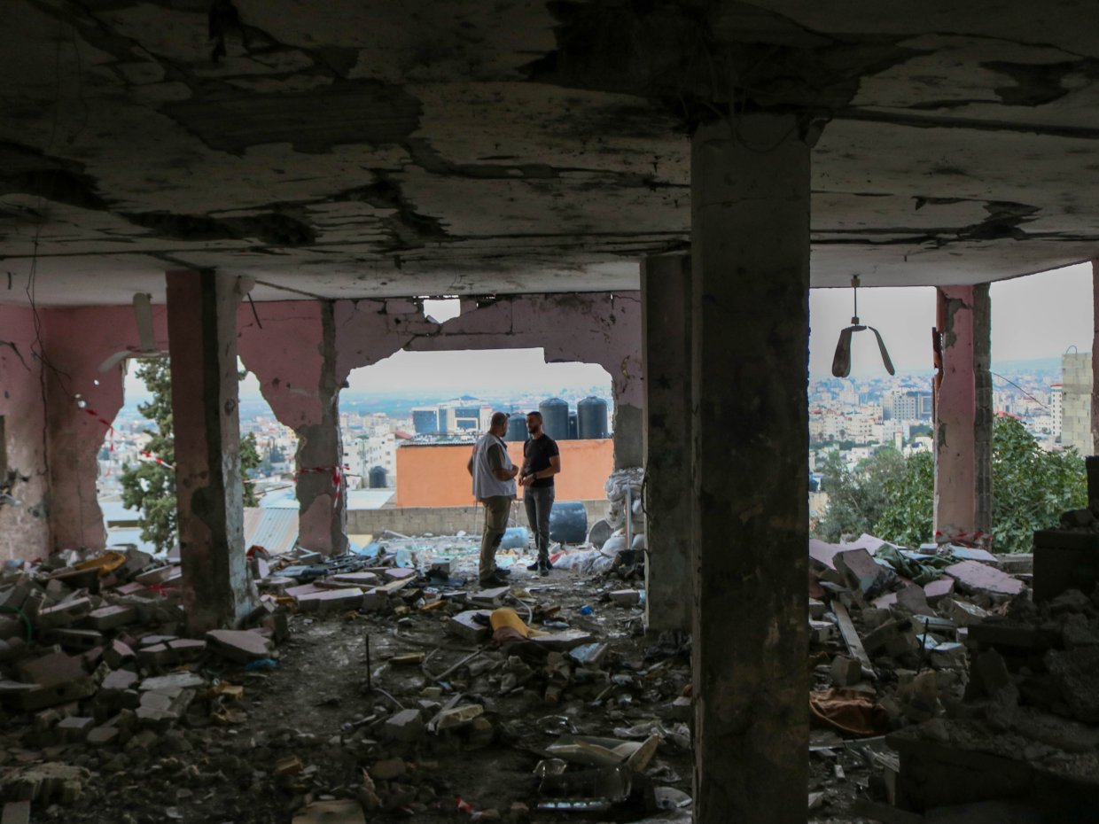 Två personer står i en byggnad där det inte finns några väggar kvar och det är massa ras omkring dem.