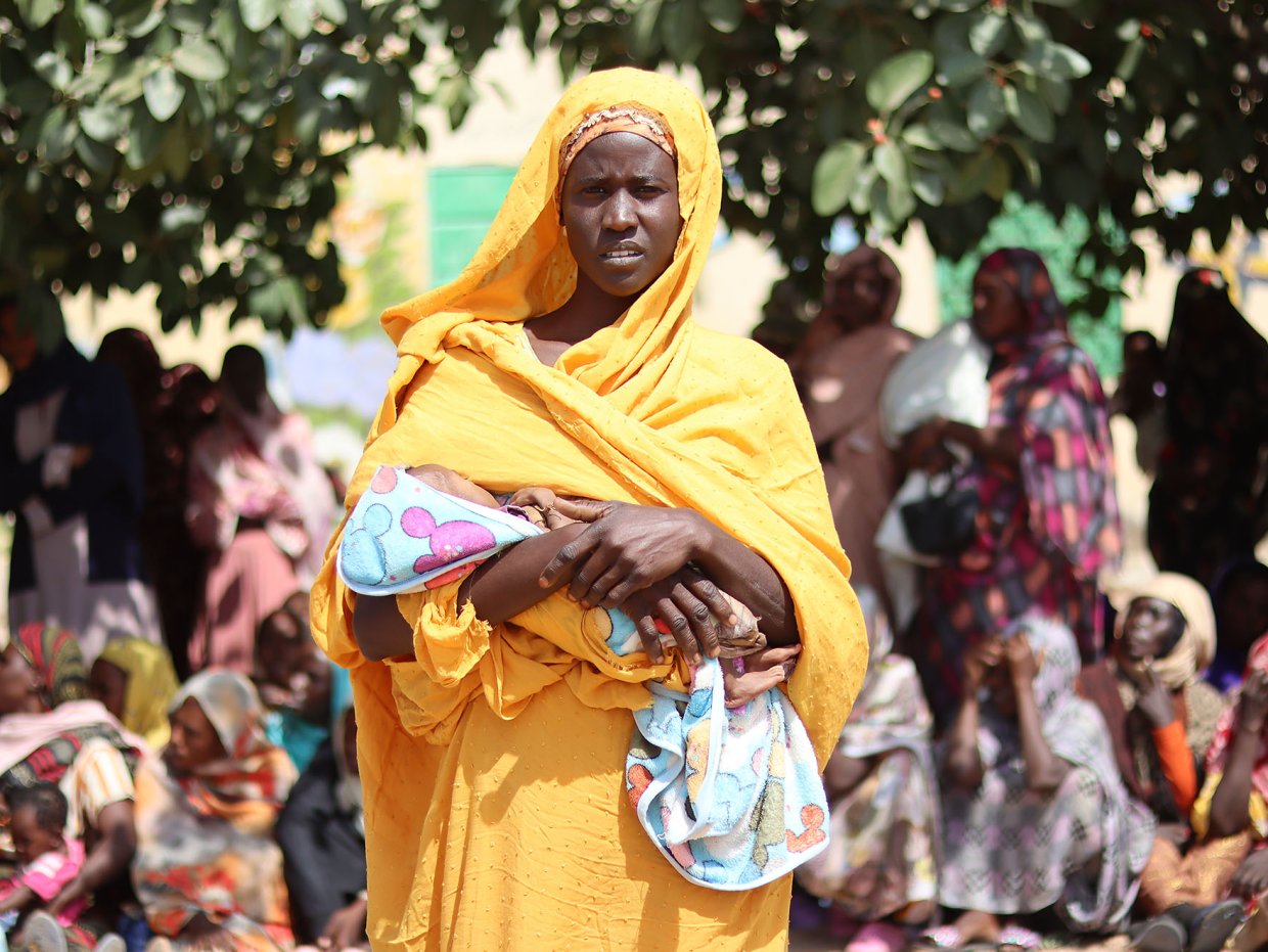 Kvinna med barn i famnen i kö för matdistribution