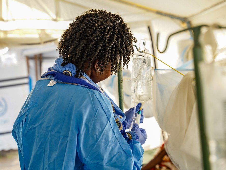 En kvinna i ljusblått syns bakifrån fixa till en droppställning.