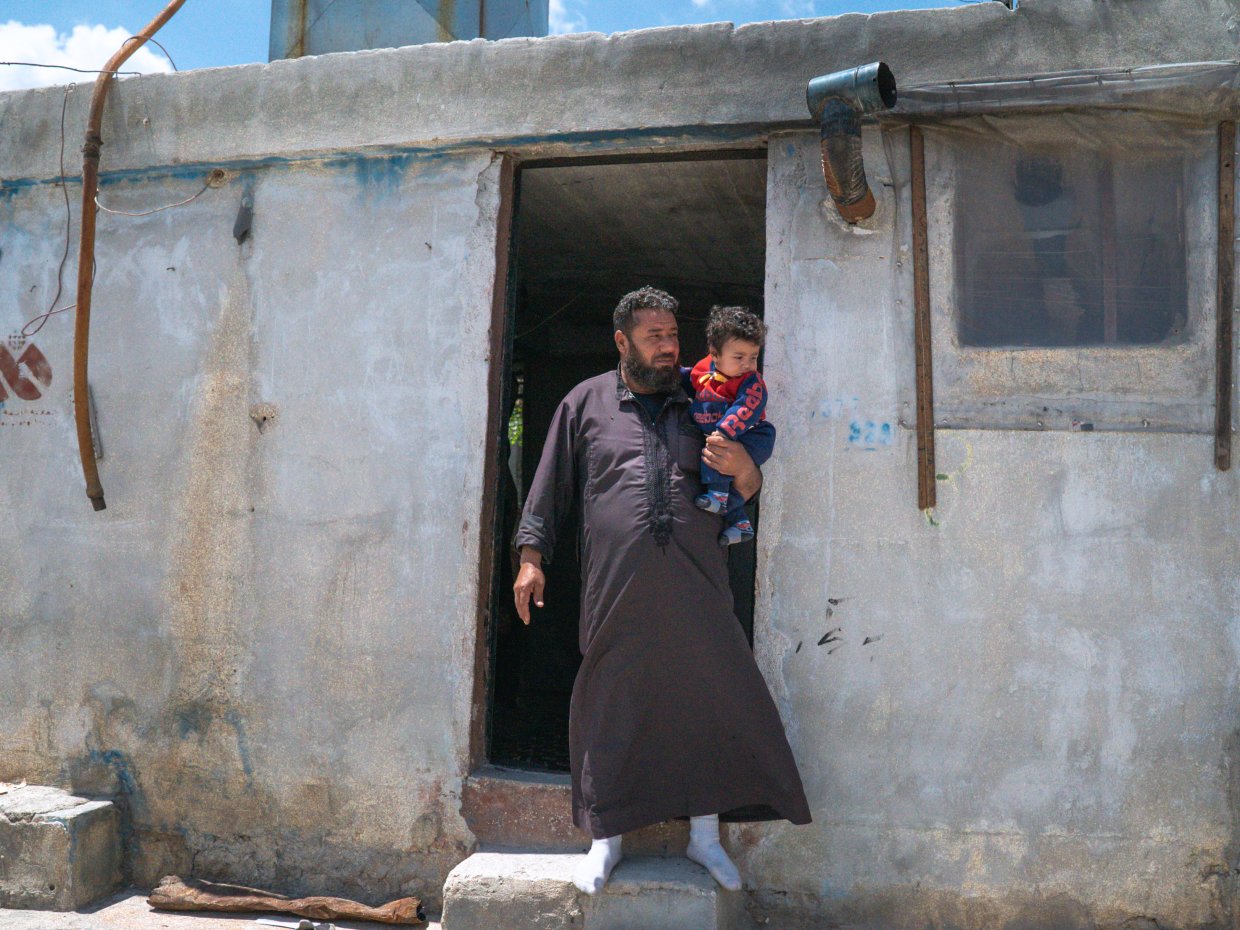 En man håller i ett barn vid en dörröppning till en cementbyggnad.
