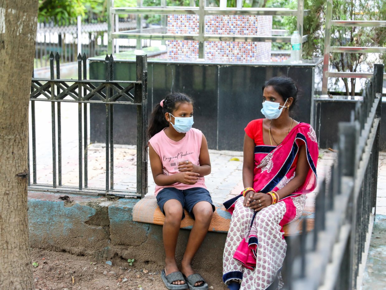 En kvinna och ett barn som sitter utomhus på en bänk. Båda två har munskydd på sig.