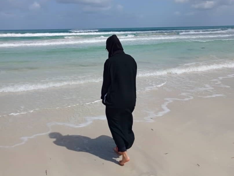 Kvinna går på en strand med ryggen mot kameran.