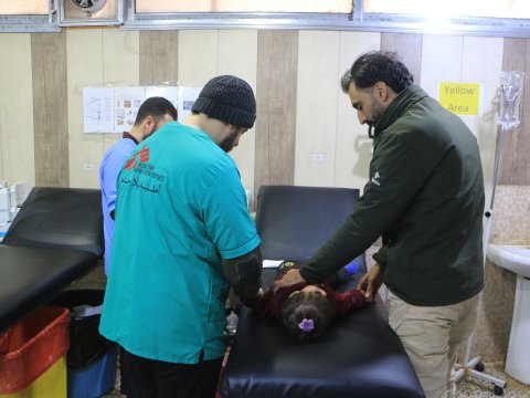 Tre män står runt en sjukhussäng som det ligger en liten flicka på. 