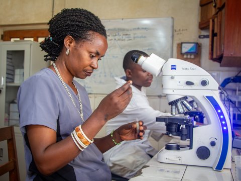 En kvinna sitter vid ett mikroskop och tyder ett provsvar.