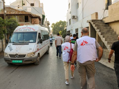 Personal från Läkare Utan Gränser går med ryggen mot kameran, förbi en ambulans.