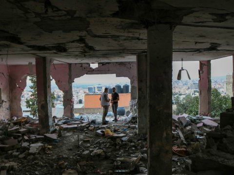 Två personer står i en byggnad där det inte finns några väggar kvar och det är massa ras omkring dem.