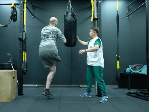 Man med amputerat ben och arm tränar boxning mot en sandsäck under överinseende av en fysioterapeut
