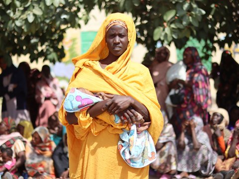 Kvinna med barn i famnen i kö för matdistribution