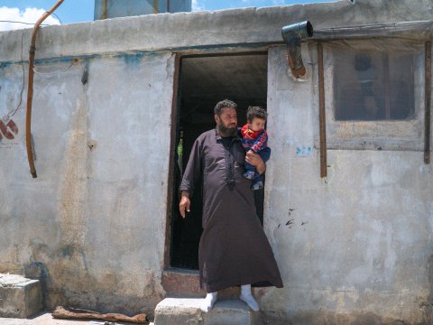 En man håller i ett barn vid en dörröppning till en cementbyggnad.