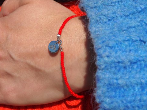 Ett rött pärlarmband på en arm med en tjocktröja