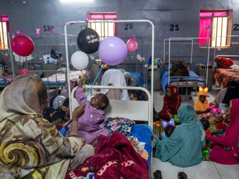 Ett barn i en säng som leker med ballonger. Bredvid barnet en kvinna som sitter på sängen.