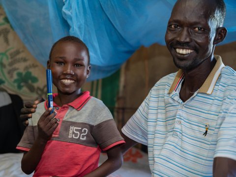 En man och ett barn som håller upp en insulinpenna och ler.