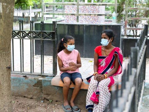 En kvinna och ett barn som sitter utomhus på en bänk. Båda två har munskydd på sig.