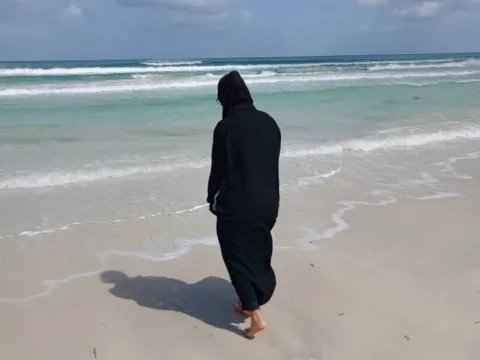 Kvinna går på en strand med ryggen mot kameran.