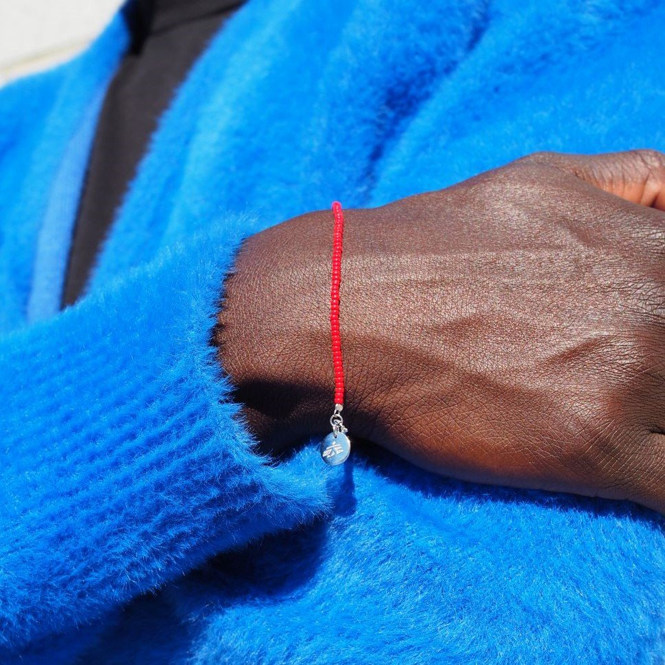 Närbild på en hand och en underarm med blå tröja bärandes ett rött pärlarmband med en silverberlock