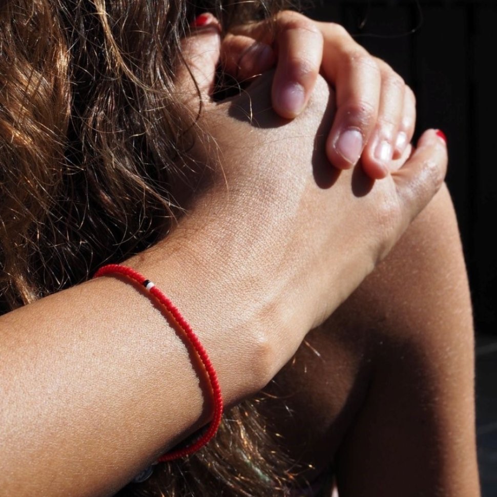 Närbild på en hand och en underarm med ett rött pärlarmband som kramar om någon