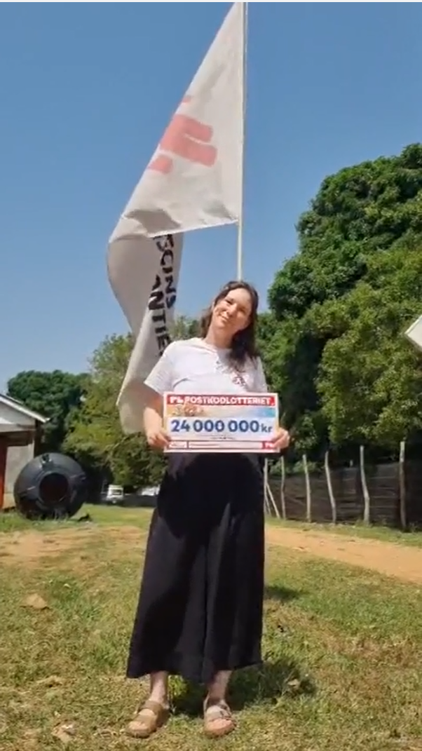 Felicia framför en Läkare Utan Gränser-flagga utomhus med en check där det står 24 miljoner