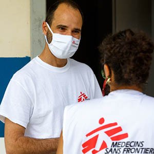 Man med svart hår har på sig en vit t-shirt med MSF-logga samt ett vitt munskydd.