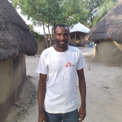 En man står framför några hus i Sydsudan och tittar in i kameran.