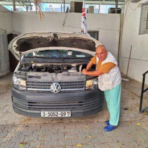 En man i vit väst meckar på en bil med öppen motorhuv