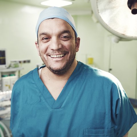En kirurg i blå läkarkläder ler mot kameran  