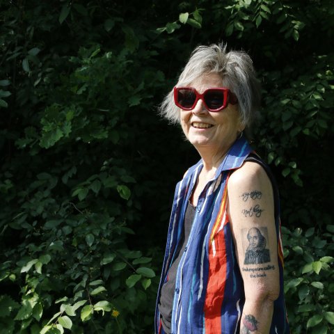 En person i stora solglasögon och många tatueringar på armen står utomhus